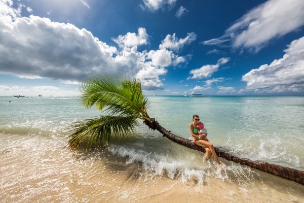 femme avec son bébé sur un palmier dans l'eau sur une plage en Guyane