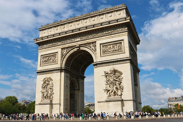 L'Arc de Triomphe à Paris sous un ciel bleu parsemé de nuages blancs, illustrant un monument emblématique de la capitale