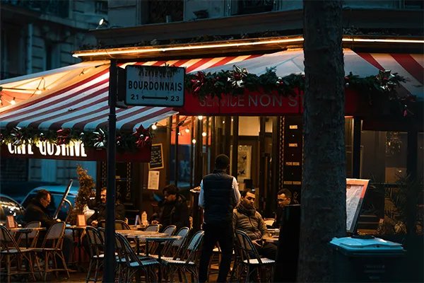 Terrasse typique d un café parisien à l angle de l Avenue de la Bourdonnais, illuminée en soirée avec ses stores rayés rouge 