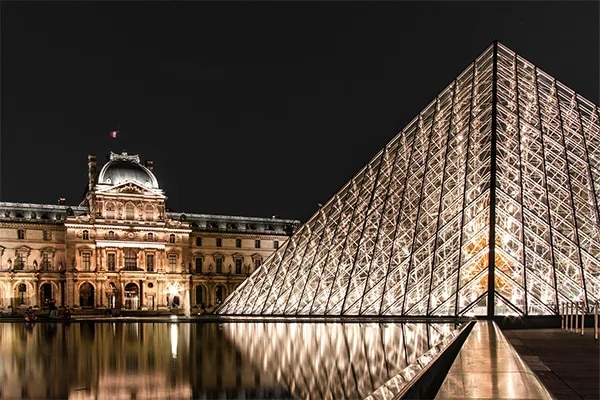 Vue nocturne de la Pyramide du Louvre illuminée avec le Palais du Louvre en arrière-plan, reflétés sur les bassins d eau sous