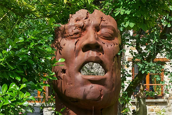 Sculpture monumentale en terre cuite représentant un visage humain expressif à la bouche ouverte, installée en plein air dans