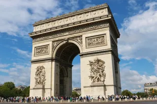 L'Arc de Triomphe à Paris sous un ciel bleu parsemé de nuages blancs, illustrant un monument emblématique de la capitale française à visiter lors d'un séjour au printemps ou en automne.