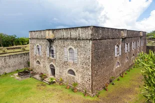 Vue extérieure du Fort Fleur d'Épée au Gosier, une imposante bâtisse historique en pierres volcaniques abritant des expositions culturelles et offrant un panorama sur la baie.