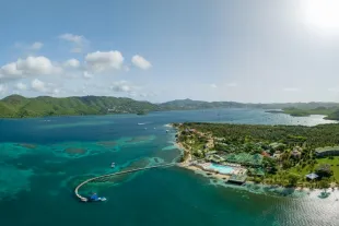 Vue aérienne panoramique du littoral martiniquais sous un ciel bleu ensoleillé, illustrant le climat tropical maritime avec une mer turquoise cristalline, une végétation luxuriante et des reliefs volcaniques en arrière-plan.