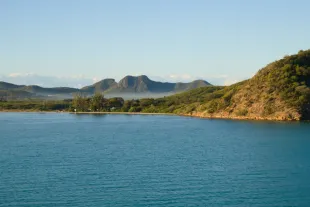 Baie aux eaux bleues bordée de collines verdoyantes sous un ciel dégagé