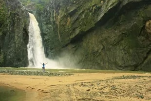 Randonneur debout devant une cascade et ses falaises.