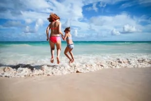 Femme et enfant s'amusant à sauter dans l'écume au bord d'une mer turquoise.